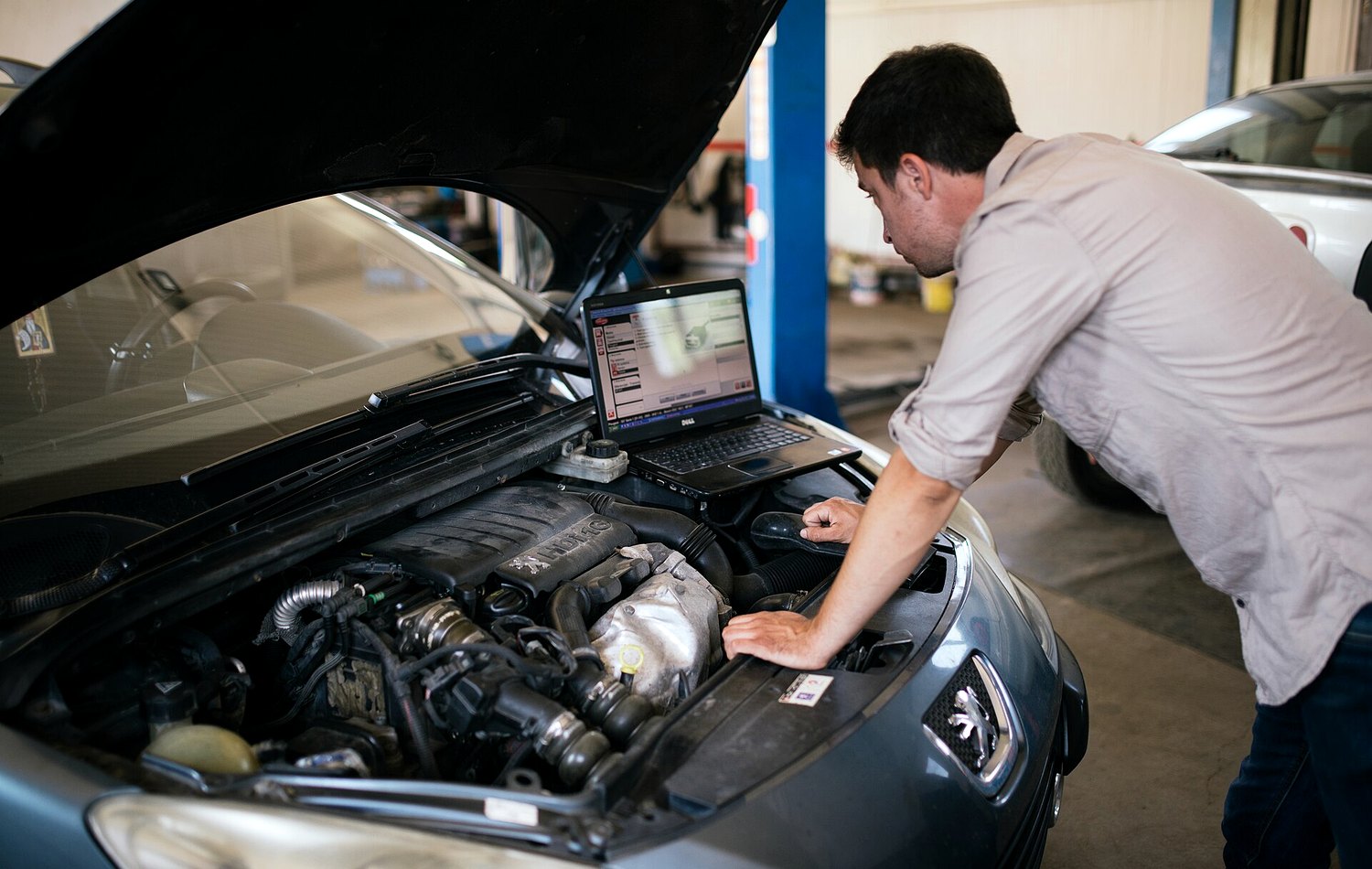 Mechanic running a vehicle diagnostic beside an open bonnet