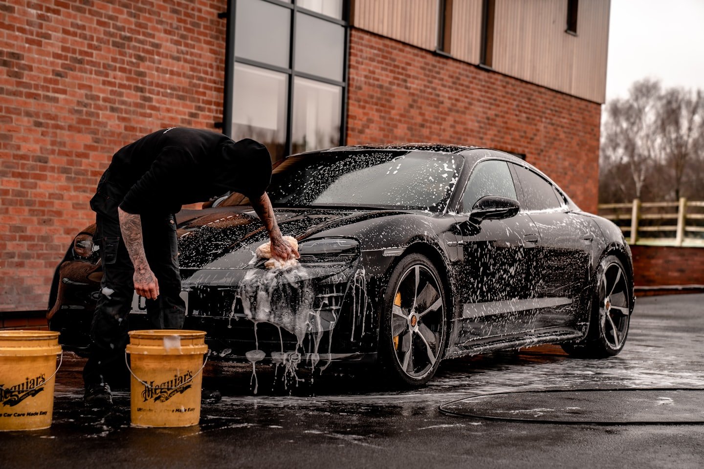 Driveway car wash with buckets and foam beside a black car